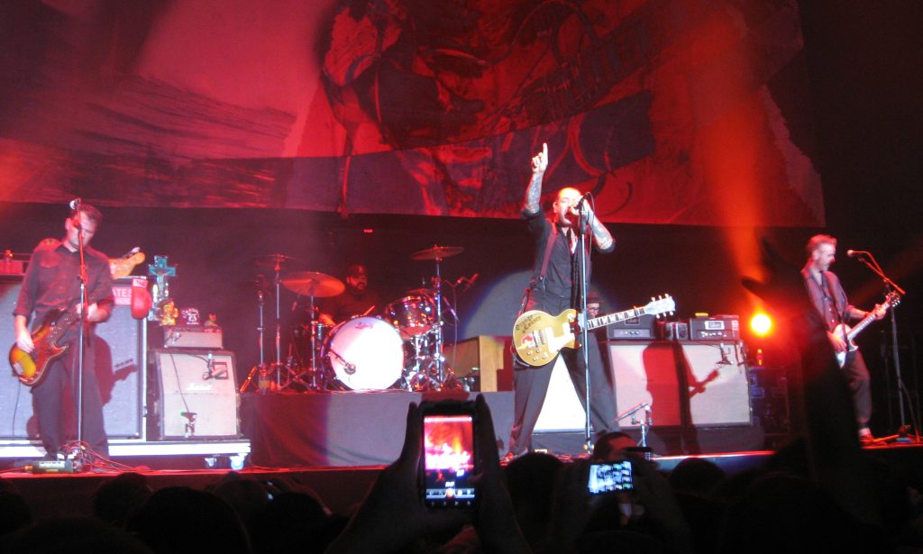 Social Distortion — Social Distortion performing at the Valley View Casino Center in San Diego, California on December 11, 2011 as part of radio station 91X's "Wrex the Halls" concert. Left to right: bassist Brent Harding, drummer David Hidalgo, Jr., singer/guitarist Mike Ness, and guitarist Jonny "2 Bags" Wickersham.